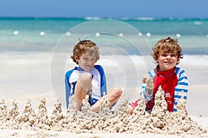 Two little kids boys having fun with building a sand castle on tropical beach of carribean island.