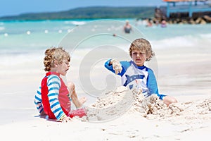 Two little kids boys having fun with building a sand castle on tropical beach of carribean island.