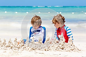 Two little kids boys having fun with building a sand castle on tropical beach of carribean island.