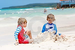 Two little kids boys having fun with building a sand castle on tropical beach of carribean island.