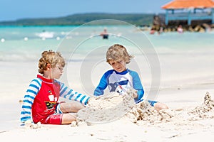 Two little kids boys having fun with building a sand castle on tropical beach of carribean island.