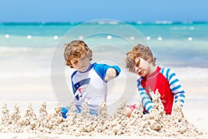 Two little kids boys having fun with building a sand castle on tropical beach of carribean island. children playing