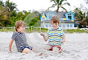 Two little kids boys having fun with building sand castle on tropical beach, happy best friends playing. Siblings