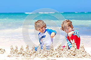 Two little kids boys having fun with building a sand castle on tropical beach on island. Healthy children playing