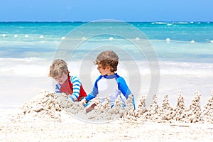 Two little kids boys having fun with building a sand castle on tropical beach of Playa del Carmen, Mexico. children