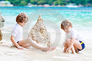 Two little kids boys having fun with building a sand castle on tropical beach of Seychelles. children playing together