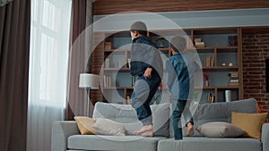 Two little kids boys jumping together on couch at living room. Funny playful active children African American siblings