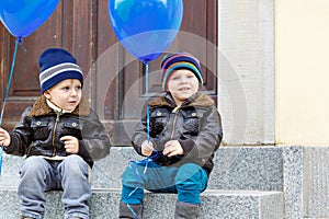 Two little kids boys playing with blue air balloons outdoors. Happy twins and toddler brothers smiling and laughing