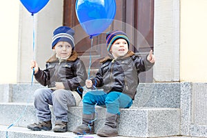 Two little kids boys playing with blue air balloons outdoors. Happy twins and toddler brothers smiling and laughing