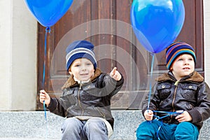 Two little kids boys playing with blue air balloons outdoors. Happy twins and toddler brothers smiling and laughing