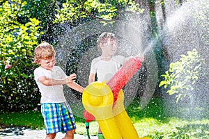 Two little kids boys playing with a garden hose water sprinkler