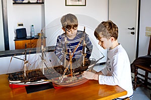 Two little kids boys playing with sailing ship model indoors. Excited children, siblings and best friends with yacht