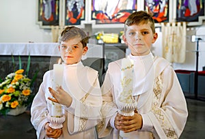 Two little kids boys receiving his first holy communion. Happy children holding Christening candle. Tradition in