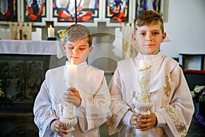Two little kids boys receiving his first holy communion. Happy children holding Christening candle. Tradition in