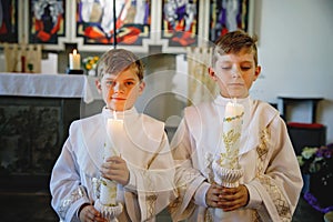 Two little kids boys receiving his first holy communion. Happy children holding Christening candle. Tradition in