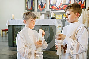 Two little kids boys receiving his first holy communion. Happy children holding Christening candle. Tradition in