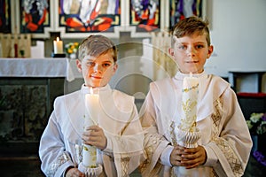 Two little kids boys receiving his first holy communion. Happy children holding Christening candle. Tradition in