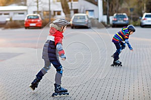 Two little kids boys skating with rollers in the city. Happy children, siblings and best friends in protection safety