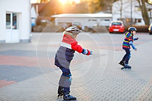 Two little kids boys skating with rollers in the city. Happy children, siblings and best friends in protection safety