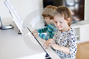 Two little kids girl and boy playing piano in living room or music school