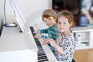 Two little kids girl and boy playing piano in living room or music school