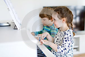 Two little kids girl and boy playing piano in living room or music school