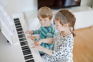 Two little kids girl and boy playing piano in living room or music school