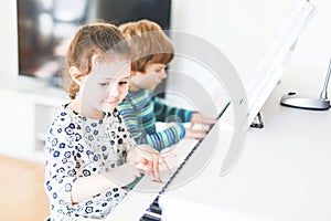 Two little kids girl and boy playing piano in living room or music school. Preschool children having fun with learning