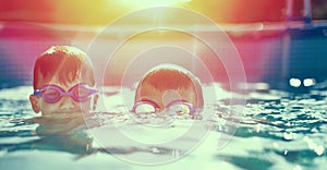 Two little kids in goggles swimming in pool at sunset