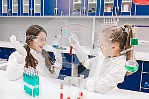 Two little kids in lab coat learning chemistry in school laboratory. Young scientists in protective glasses making