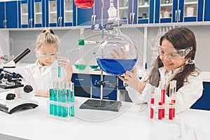 Two little kids in lab coat learning chemistry in school laboratory. Young scientists in protective glasses making