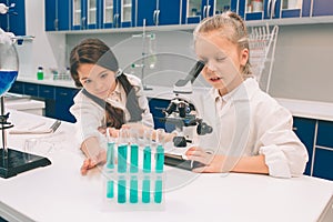 Two little kids in lab coat learning chemistry in school laboratory. Young scientists in protective glasses making