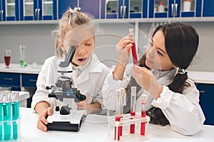 Two little kids in lab coat learning chemistry in school laboratory. Young scientists in protective glasses making