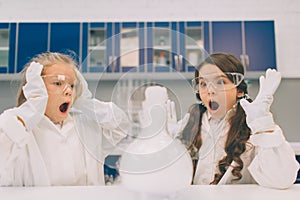 Two little kids in lab coat learning chemistry in school laboratory. Young scientists in protective glasses making