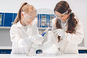 Two little kids in lab coat learning chemistry in school laboratory. Young scientists in protective glasses making