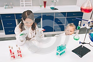 Two little kids in lab coat learning chemistry in school laboratory. Young scientists in protective glasses making