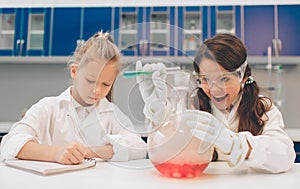 Two little kids in lab coat learning chemistry in school laboratory. Young scientists in protective glasses making