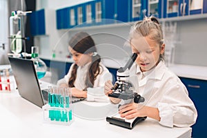 Two little kids in lab coat learning chemistry in school laboratory. Young scientists in protective glasses making