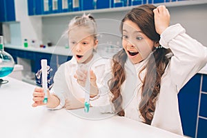 Two little kids in lab coat learning chemistry in school laboratory. Young scientists in protective glasses making