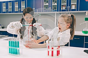 Two little kids in lab coat learning chemistry in school laboratory. Young scientists in protective glasses making