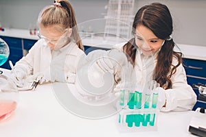 Two little kids in lab coat learning chemistry in school laboratory. Young scientists in protective glasses making