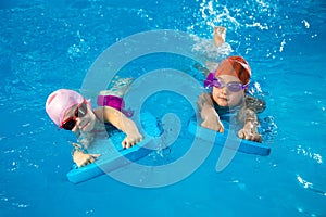 Two little kids learning how to swim in swimming pool using flutter boards