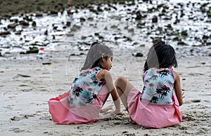 Two little kids making sand castle and playing at tropical beach. Little girls back view while playing sand on a beach