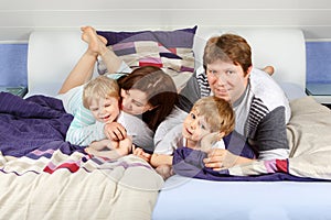 Two little kids and parents having fun in bed