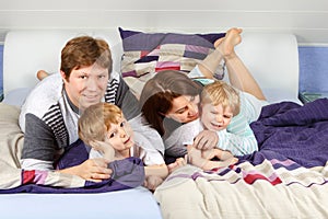 Two little kids and parents having fun in bed