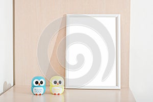 two little owl statues next to white empty frame on a bedside table in kids room. copy space for inscription