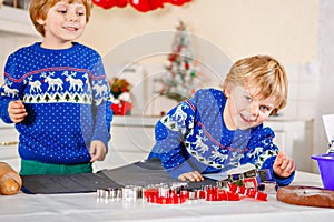 Two little preschool boys baking gingerbread cookies. Happy siblings, children in xmas sweaters. Kitchen decorated for