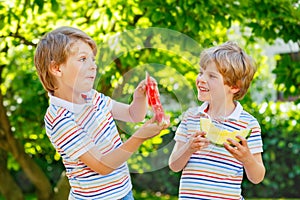Two little preschool kid boys with blond hairs eating red and yellow watermelon in summer garden. Funny happy children