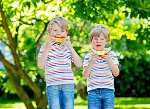 Two little preschool kid boys eating red and yellow watermelon in summer garden. Funny happy children smiling, with