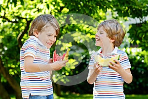 Two little preschool kid boys eating red and yellow watermelon in summer garden. Funny happy children smiling, with